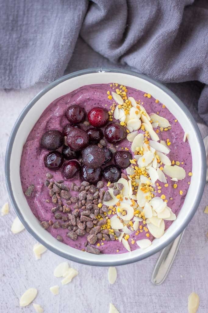 Creamy blueberry smoothie in a bowl topped with fresh berries and chopped nuts.