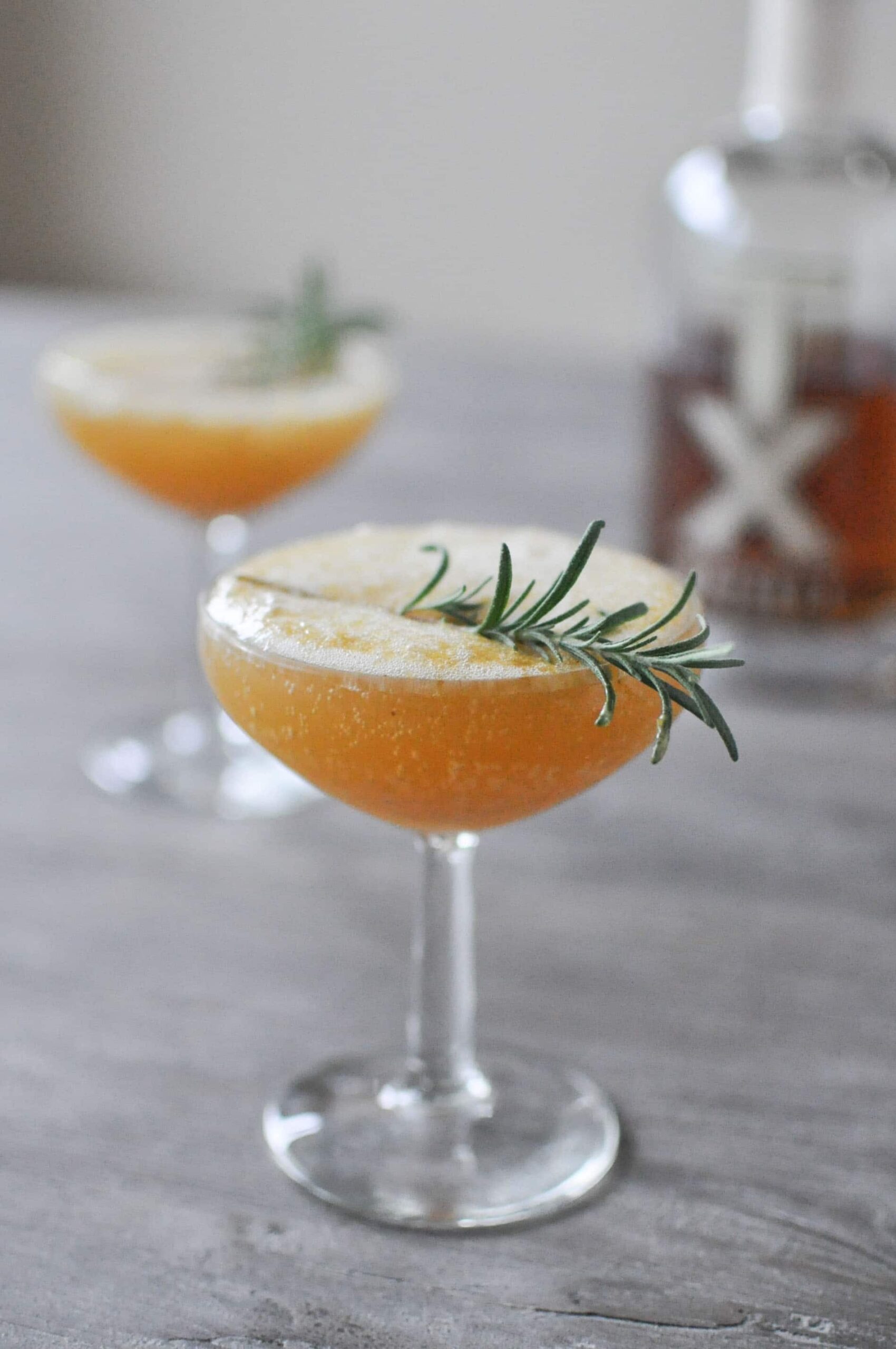 A glass of cocktail garnished with a sprig of rosemary in a glass.