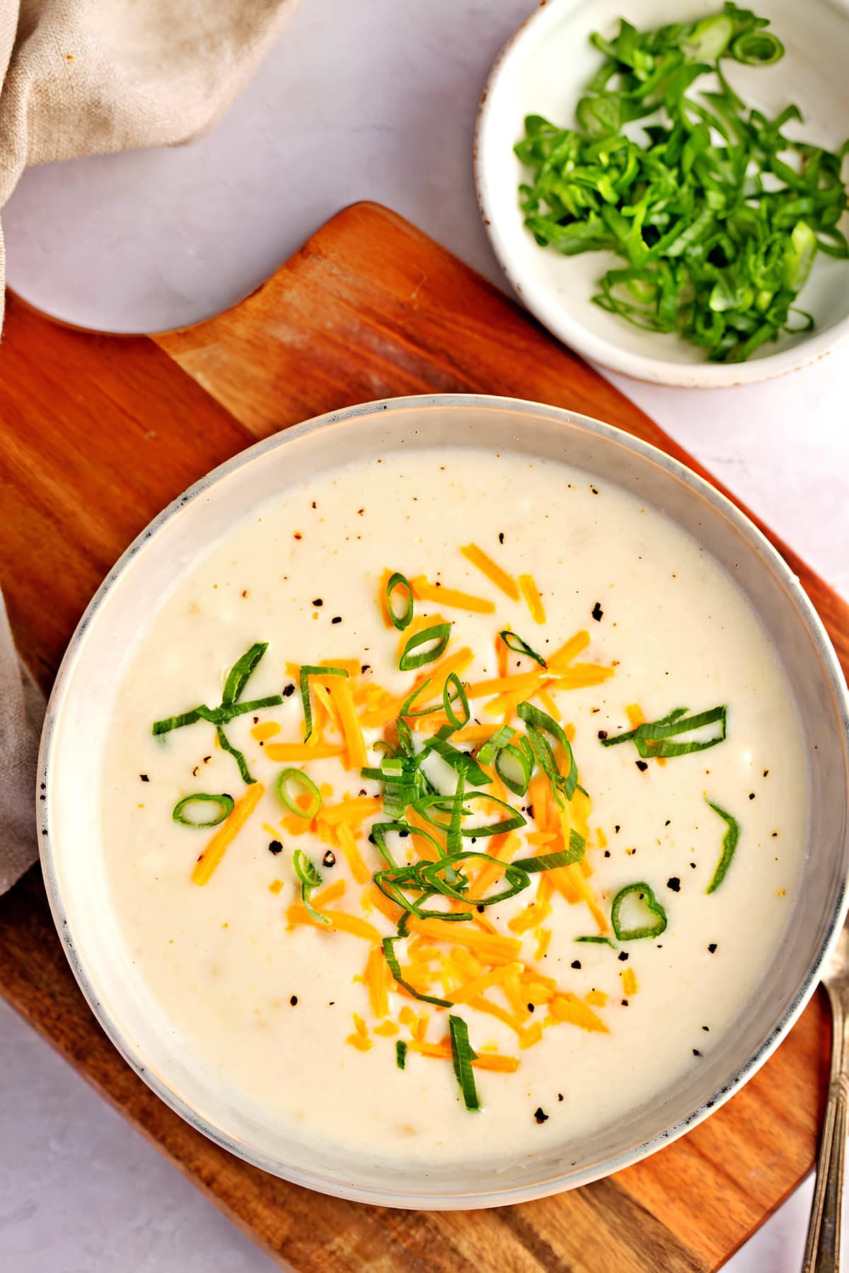 Bowl of Panera bread potato soup garnished with grated cheese and chopped onion leaves.