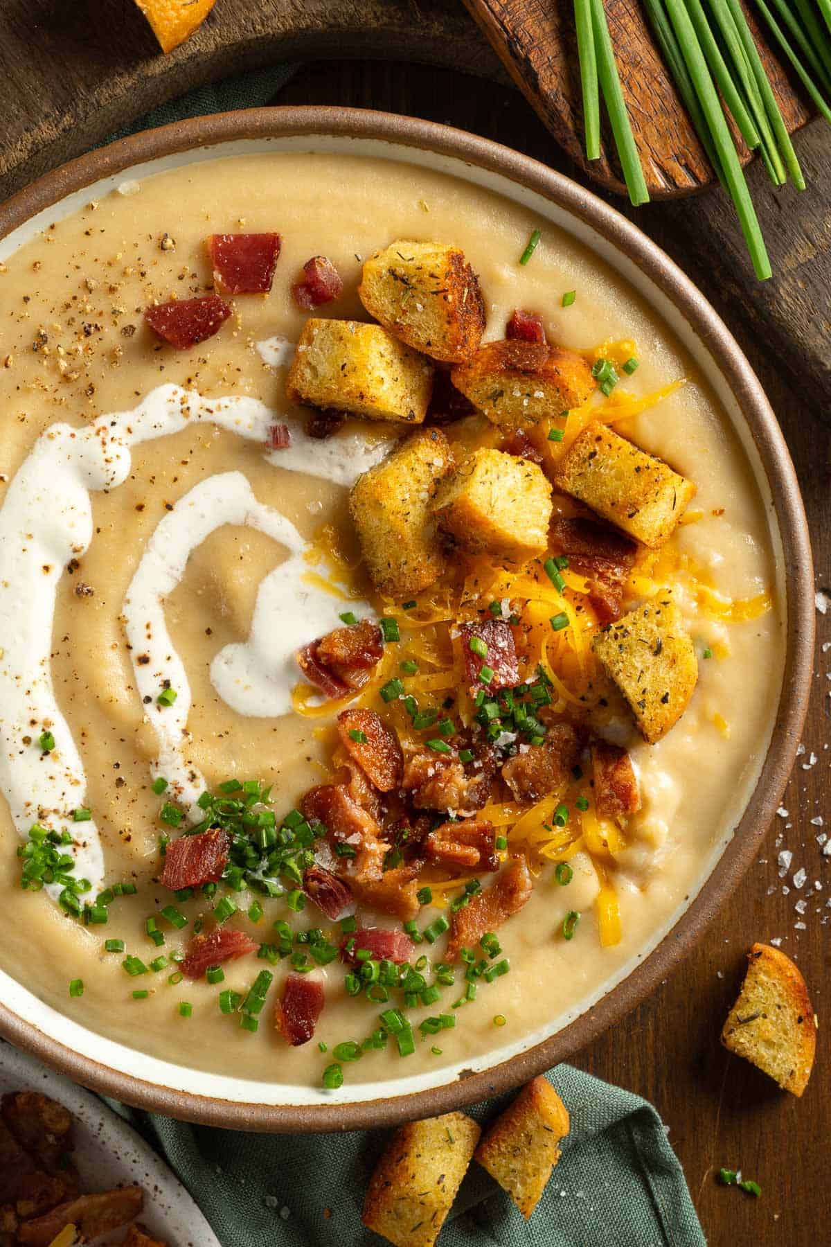 Comforting homemade potato soup with bacon, cheese green onions, croutons, and sour cream in a large clay bowl