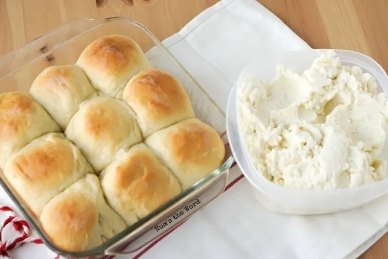 Bread rolls in a glass dish and mashed potatoes in a container on its side. 