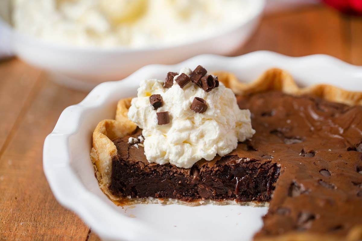 Brownie pie with a portion missing on a casserole dish topped with cream and chocolate chips.