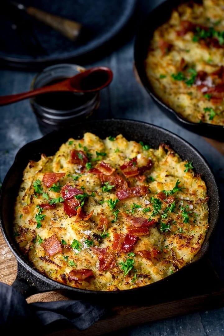 Mashed potato cooked with bacon and egg on a cast iron pan topped with chopped parsley. 