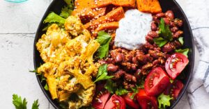 Buddha bowl full of vegetables including tomatoes and cauliflower with yogurt sauce