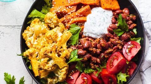 Buddha bowl full of vegetables including tomatoes and cauliflower with yogurt sauce