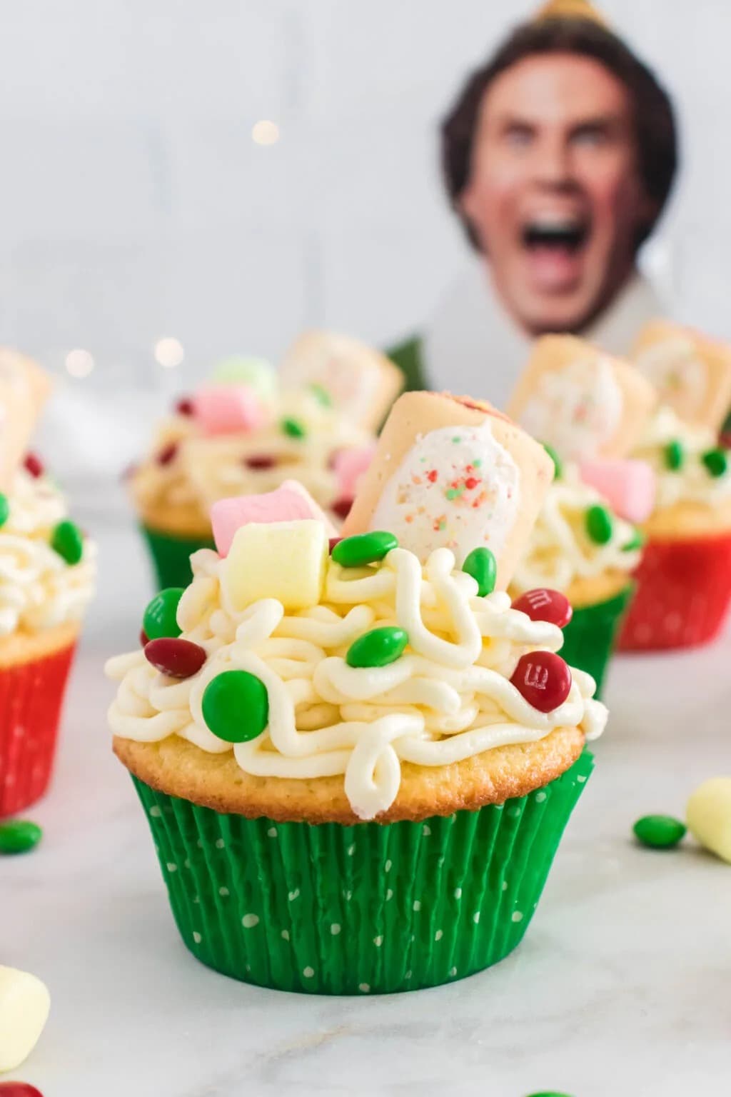 Cupcakes topped with  frosting that looks like spaghetti, candy (Christmas M&M’s), and mini marshmallows. 