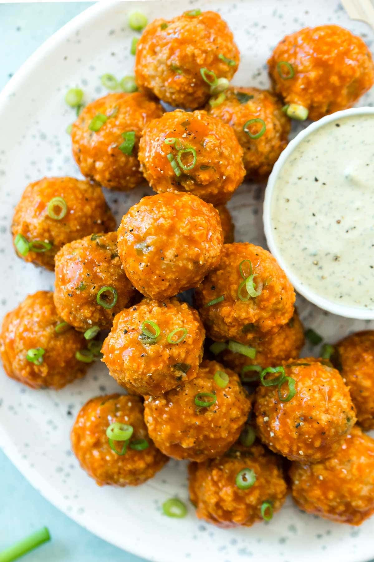 Meatballs coated with buffalo sauce served with creamy dip and garnished with chopped parsley leaves.
