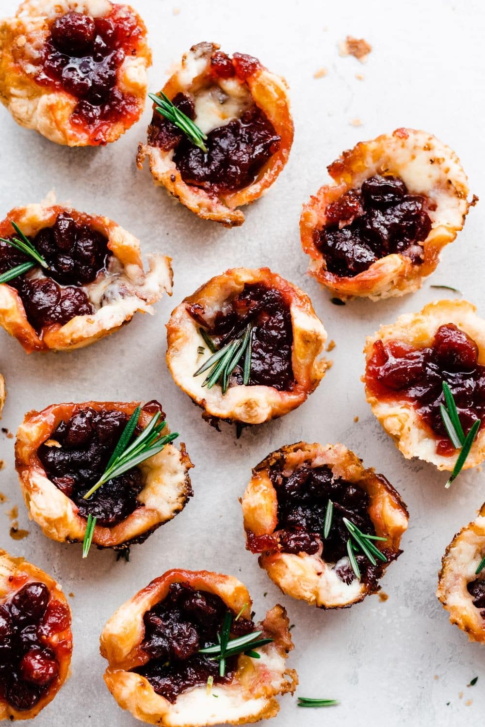 Bunch of cranberry brie bites arranged on a white table garnished with rosemary leaves.