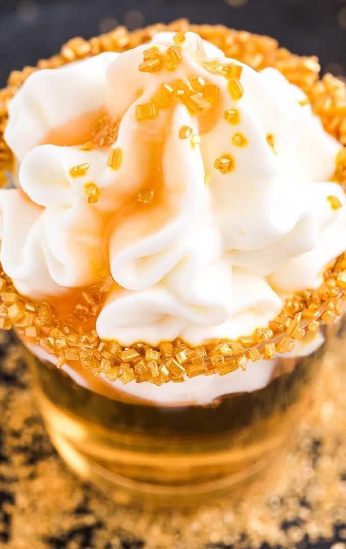 Butterbeer Jello shots on plastic cup with gold sprinkles on the rim topped with whipped cream. 