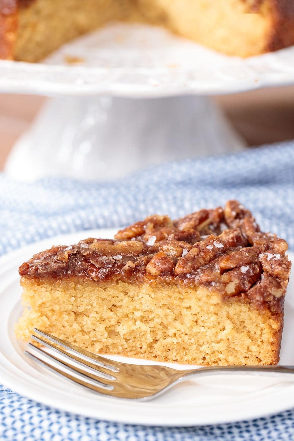 Slice of buttermilk cake with buttery pecan glaze on top served on a plate with stainless fork