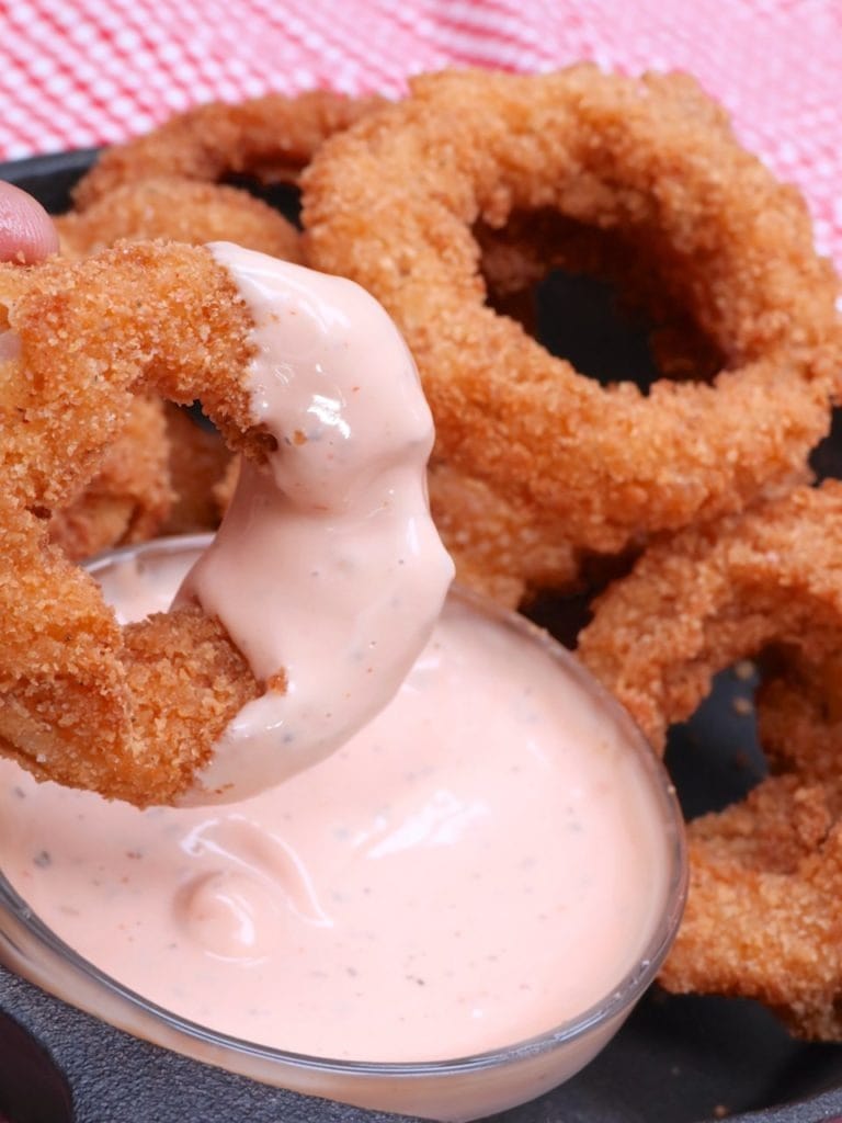 Onion ring dipped into a bowl ok mayo and ketchup dipping sauce