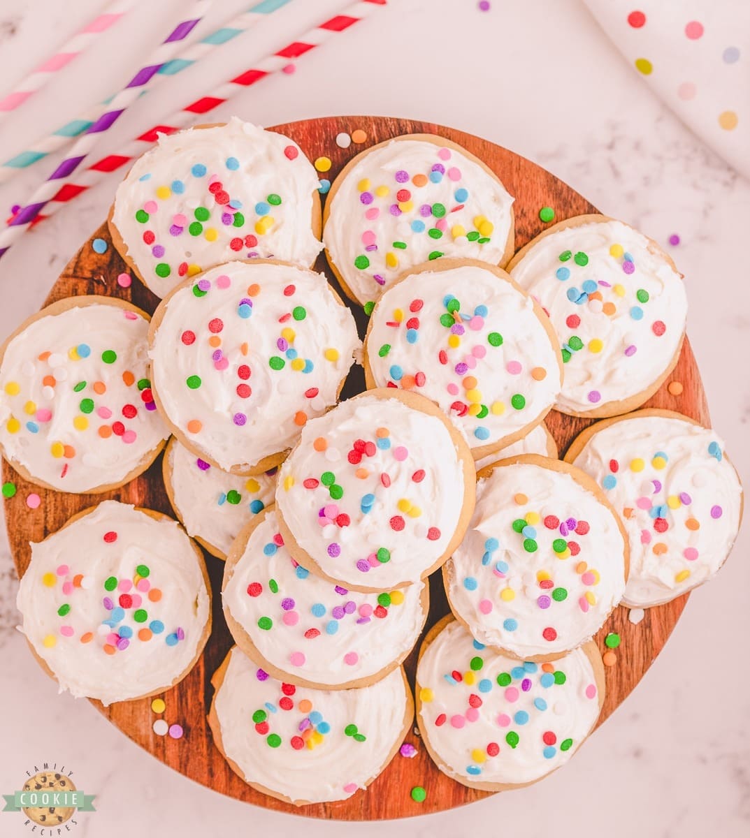 Bunch of cookies with vanilla frosting and colorful sprinkles on top served on a wooden board