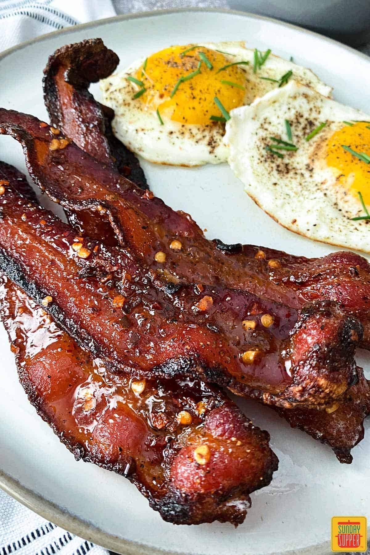 Glazing season strips of fried bacon served with sunny side egg on a plate. 