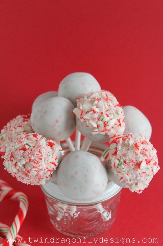 Bunch of chocolate covered cake pops on stick dipped in sprinkles arranged on a small glass. 