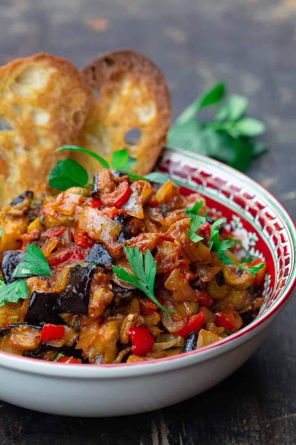 Caponata in a bowl made with eggplant, onions, tomato and olives. 