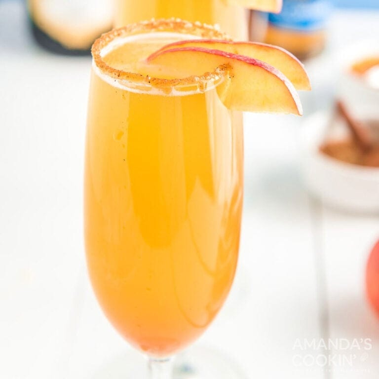 Caramel Apple Cider Mimosas in champagne flutes on a white table.