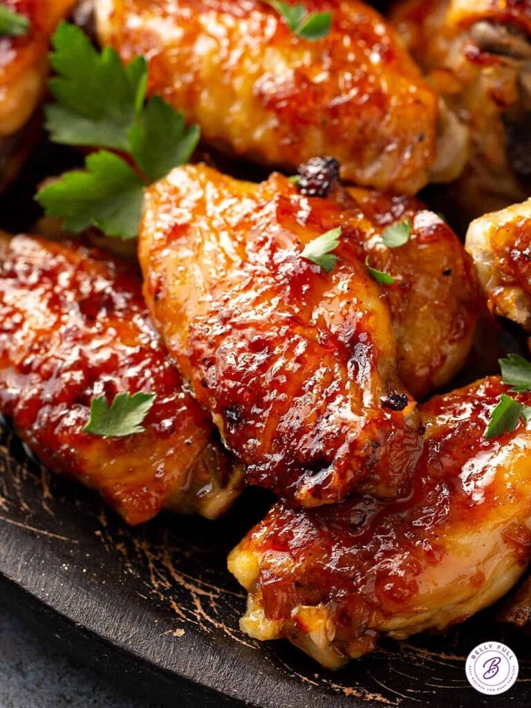 Glazed chicken wings covered with sauce served on top of a wooden tray. 
