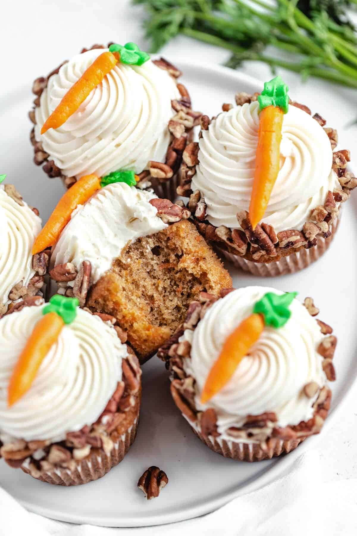 Bunch of carrot cupcake and cream cheese frosting with candy carrot garnish on top.