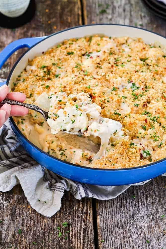 Spoon scooping cheesy cauliflower casserole on a pan. 