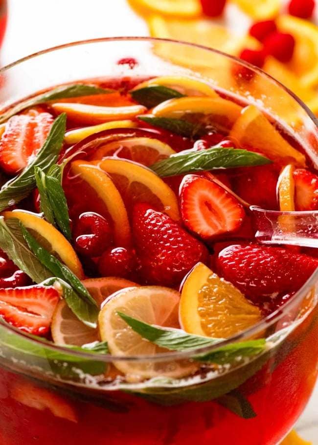 A refreshing bowl of fruit punch with vibrant fresh fruit and a hint of mint leaves.