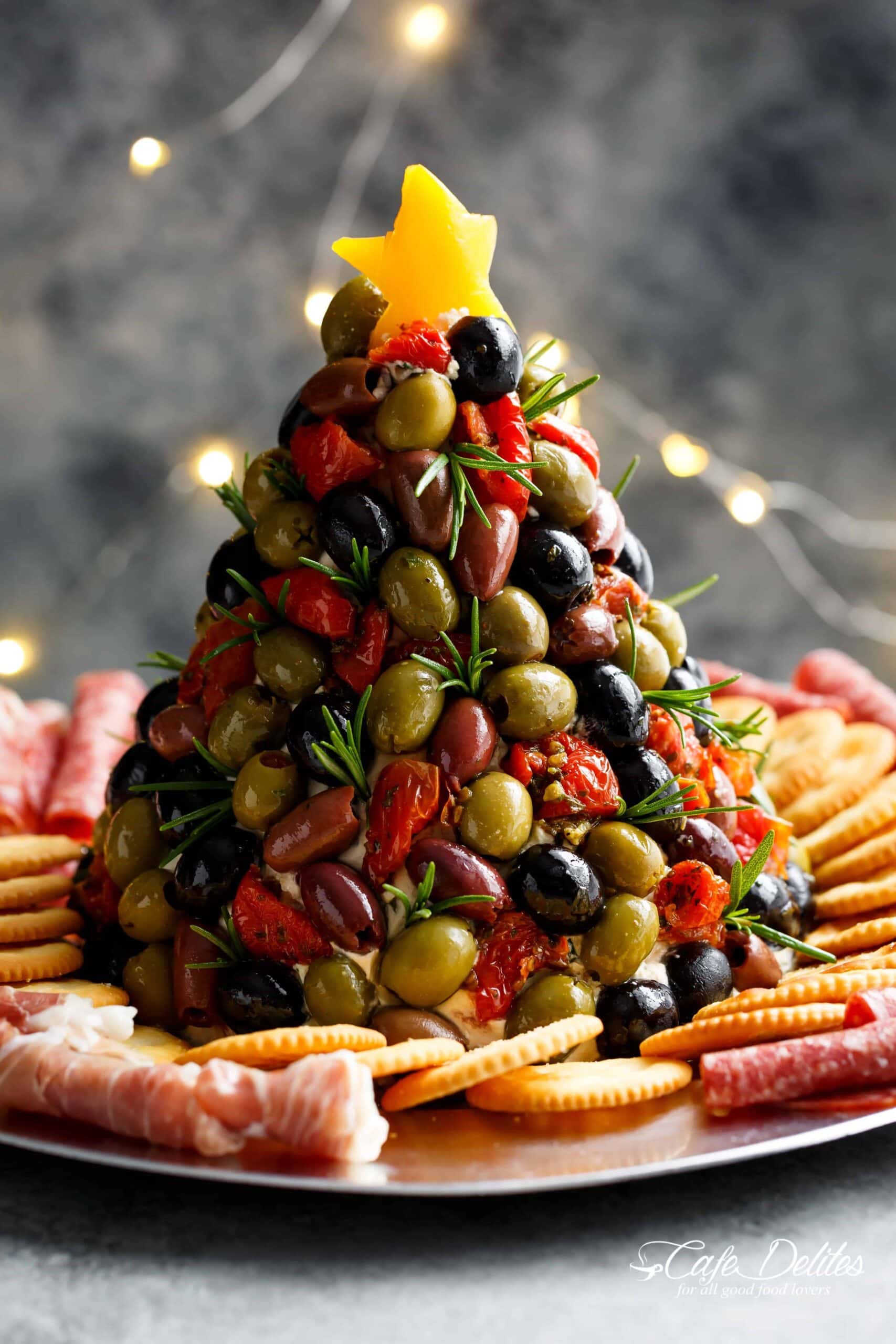Cheeseball shaped in Christmas tree covered with olives and chiles served with crackers and bologna. 