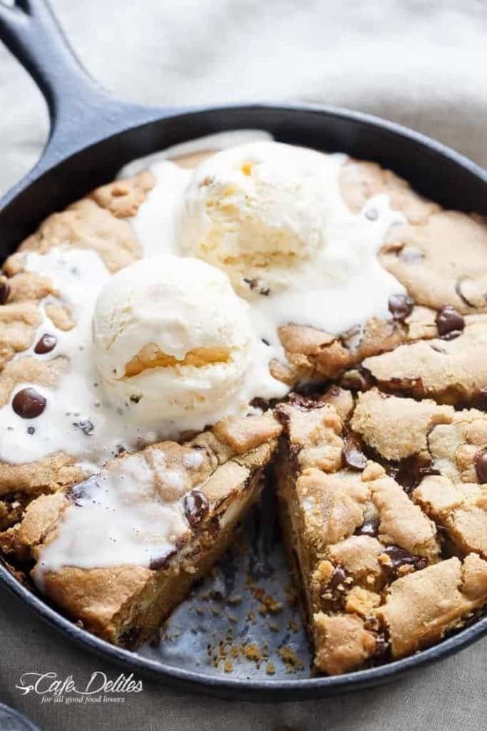 Slice missing cookie baked in a skillet topped with melting vanilla ice cream.