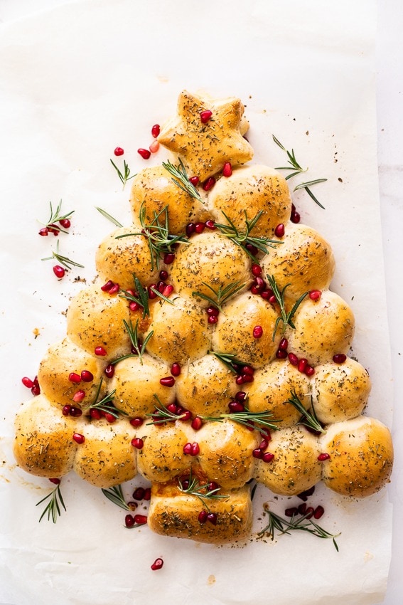 Christmas tree shaped pull apart bread garnished with pomegranate arils and rosemary sprigs.