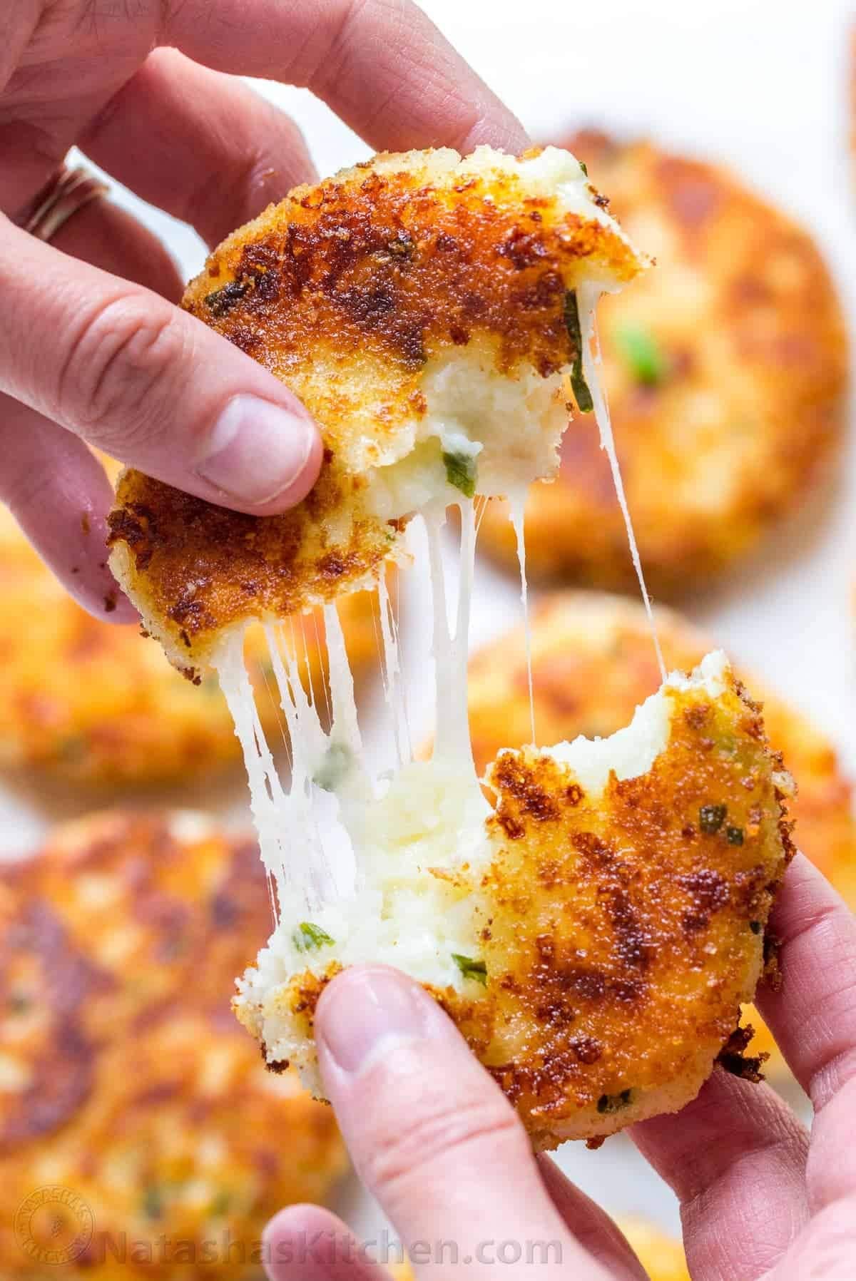 Hand pulling apart a potato ball with gooey mozzarella cheese filling. 