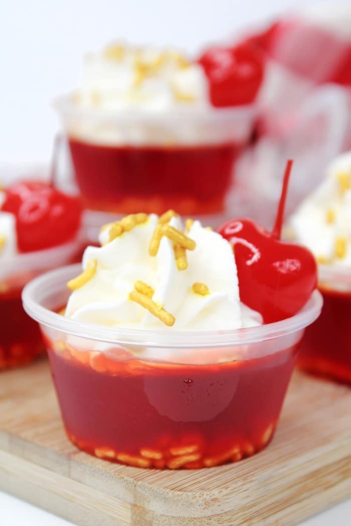 Cherry bomb Jello shots on plastic with whipped cream, gold sprinkles and fresh cherries on top. 