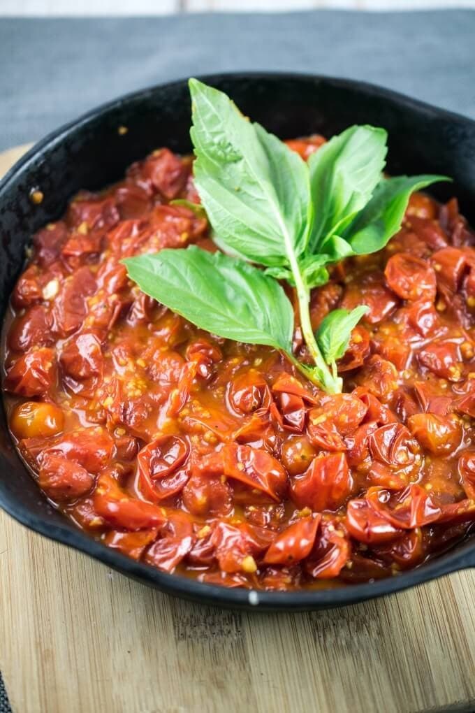 Cherry tomato sauce cooked on a skillet pan garnished with fresh basil leaves.