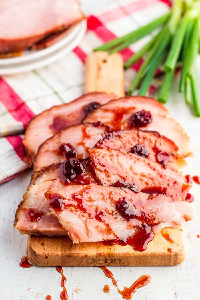 Sliced ham with drizzle of cherry glaze on a wooden board. 