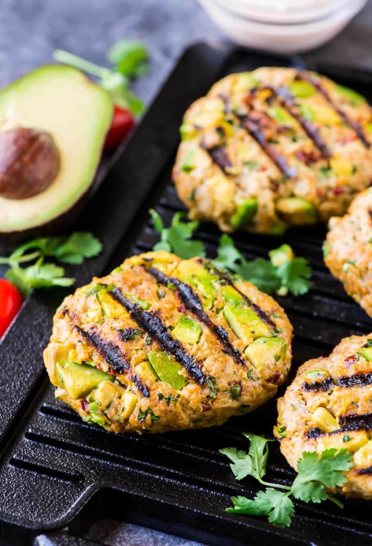 Patty with avocado slices on a grill pan.
