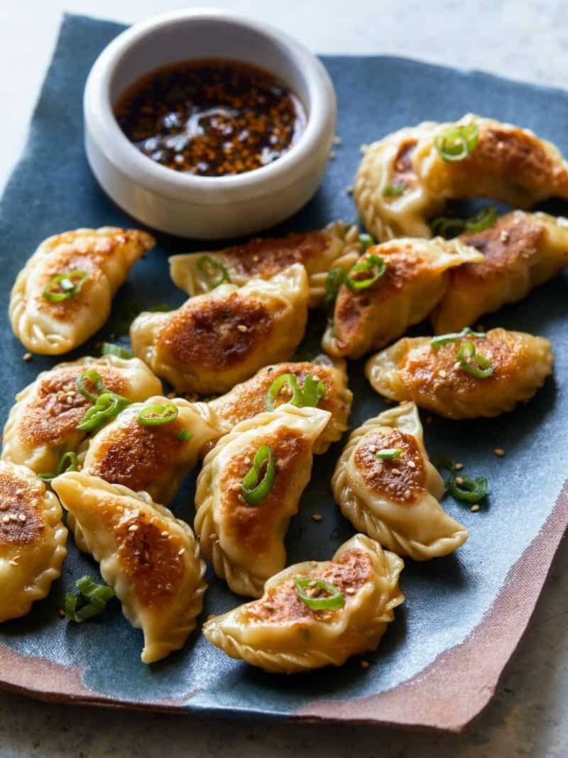 Dumplings garnished with sesame seeds and chopped onion chives with dipping sauce on sides. 