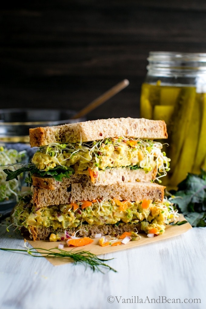 A pile of sliced chickpea salad sandwich with sprouts, kale, lettuce and carrots filling.  