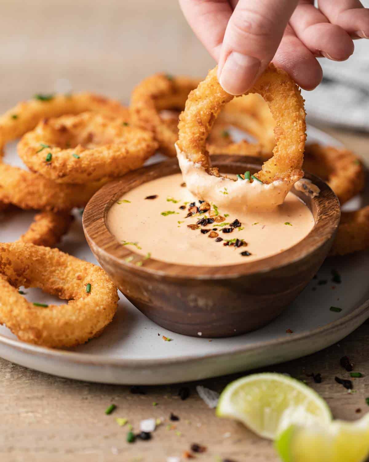 Dipping fried onion rings into a bowl of chipotle crema sauce