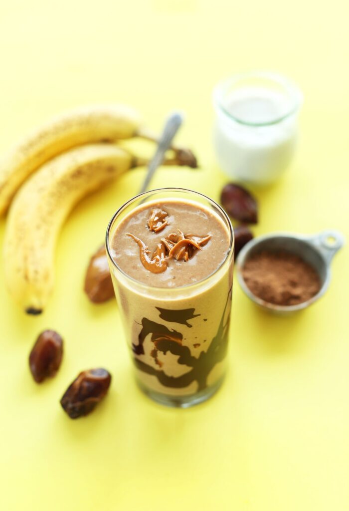 Chocolate flavored shake in a glass beside fresh bananas and nuts in the table.