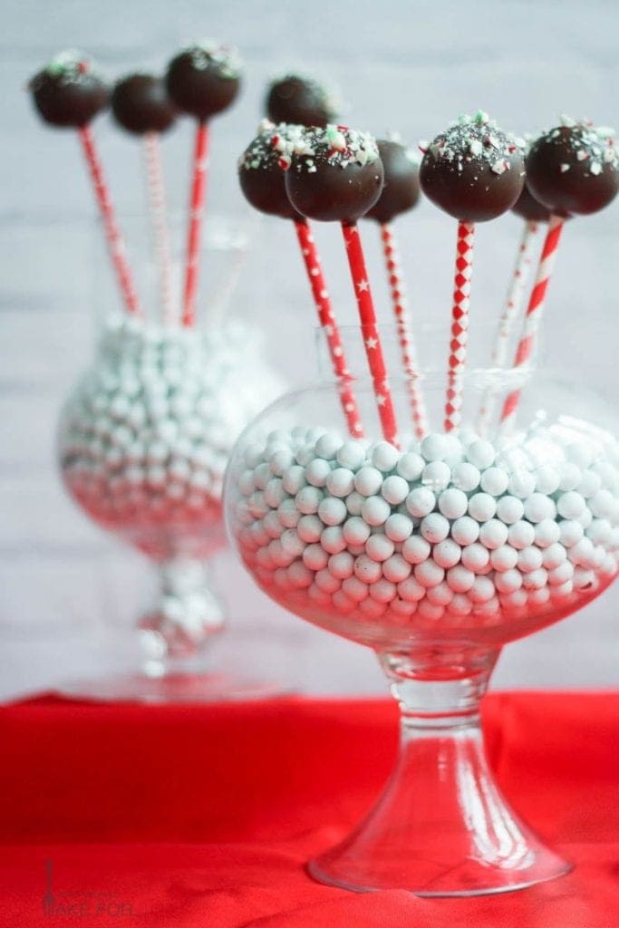 Chocolate covered cake pops on stick dipped in crushed peppermint candies arranged on a holiday table. 