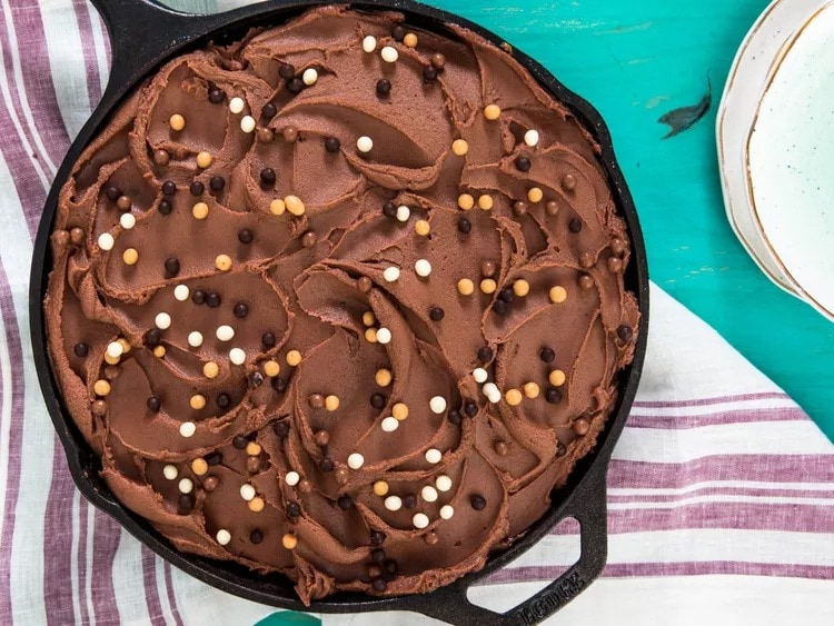 Chocolate cake cooked in a cast iron skillet topped with chocolate frosting and sprinkles. 
