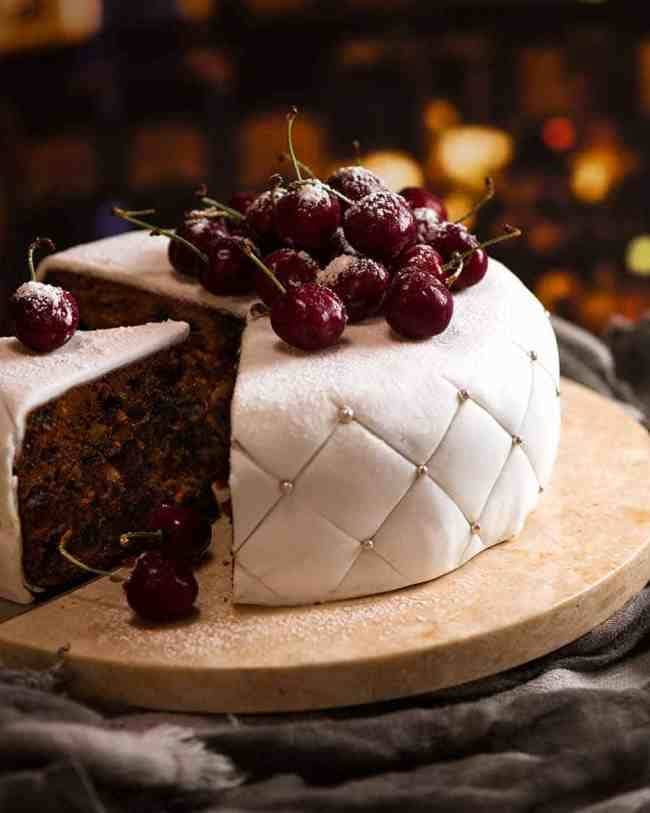 White frosted covered fruit cake topped with fresh cherries. 
