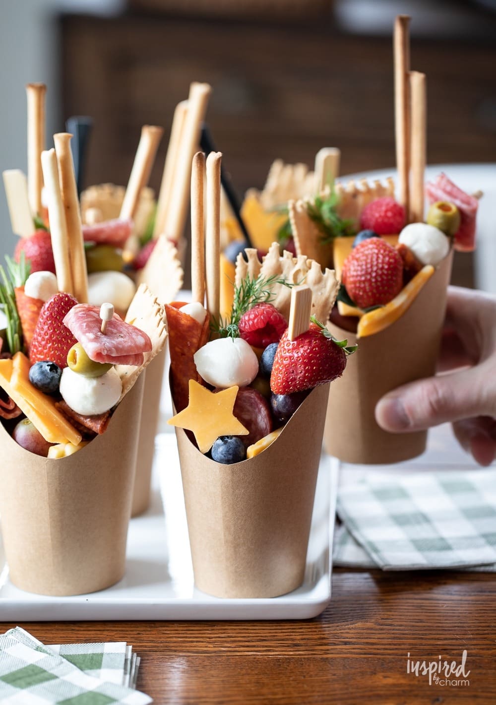 Meats, cheeses, fruits, and nuts on skewers served on paper cups.