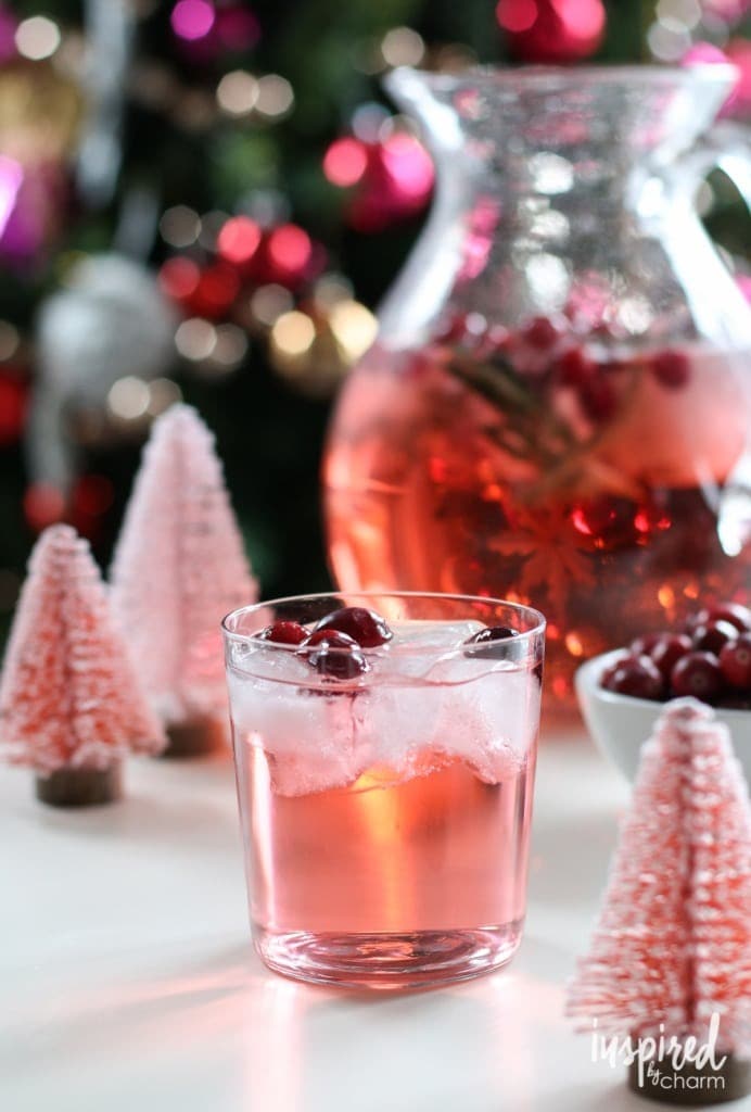 A glass of pink cocktail with ice and cranberries.