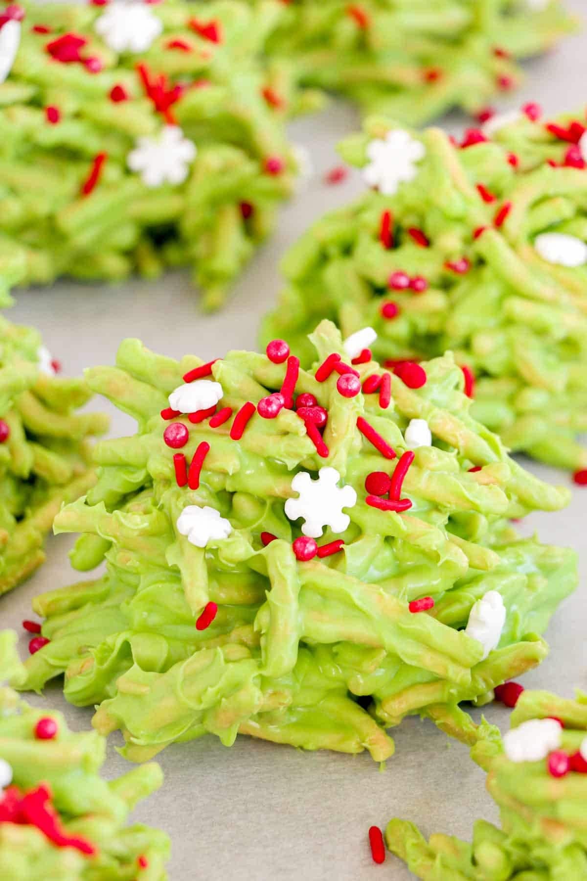 Green colored haystack cookies garnished with red and white sprinkles.