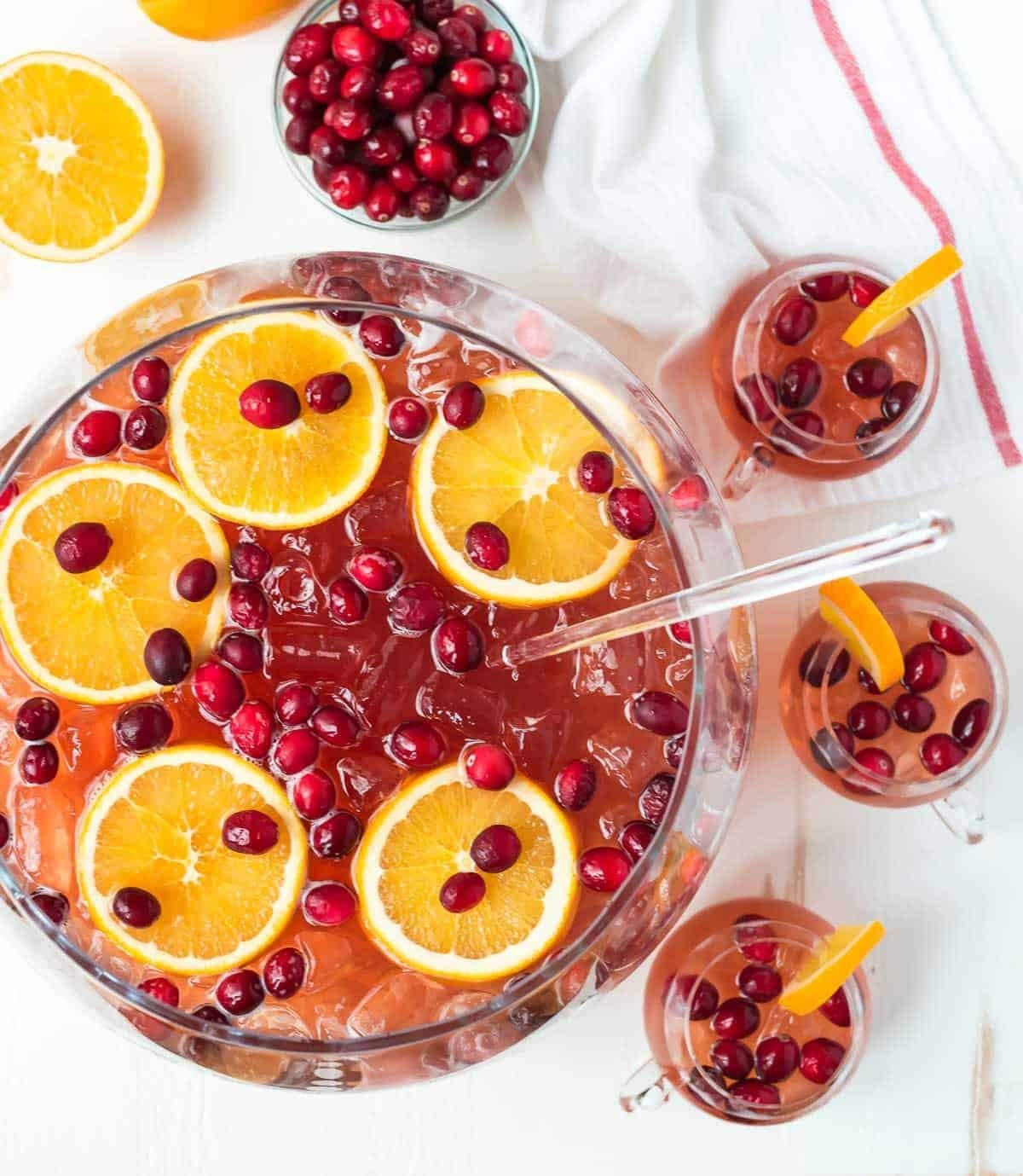 Christmas punch on a huge glass bowl with plenty of ice, fresh cranberries, and orange slices.