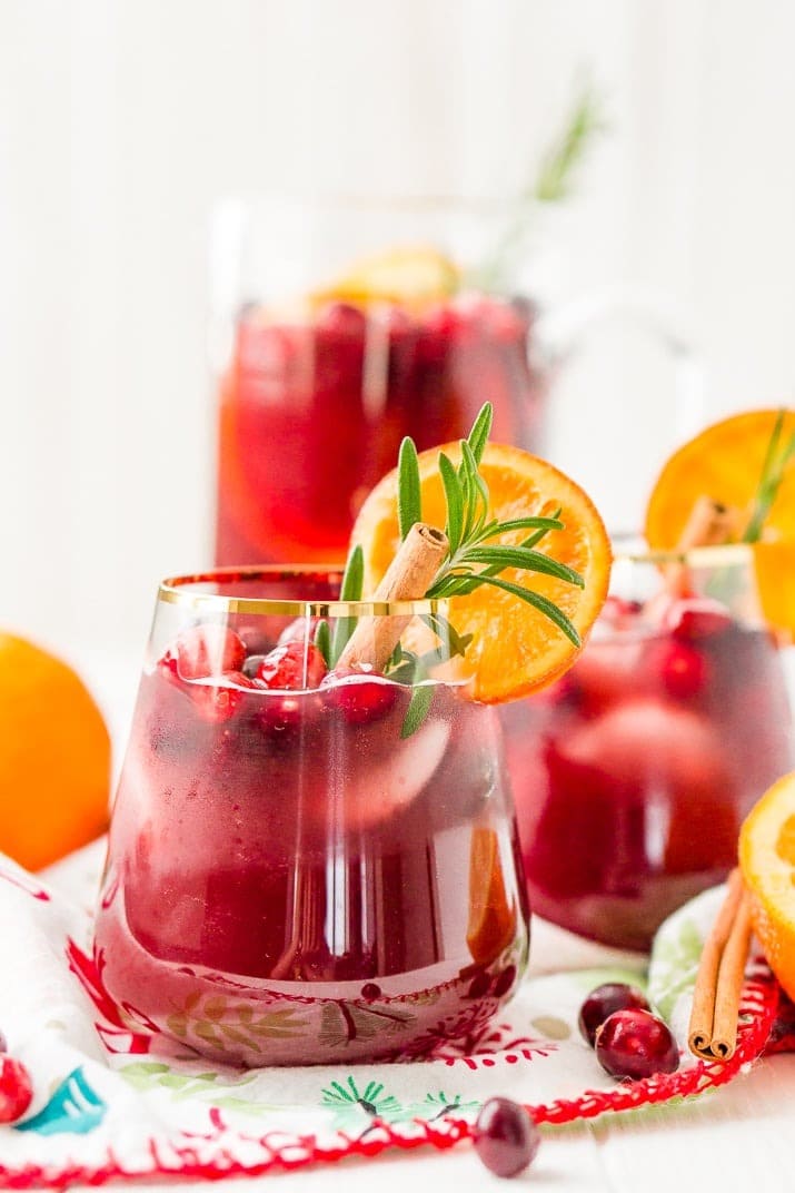 Red sangria cocktail on a glass garnished with fresh cranberries, orange slice and cinnamon. 
