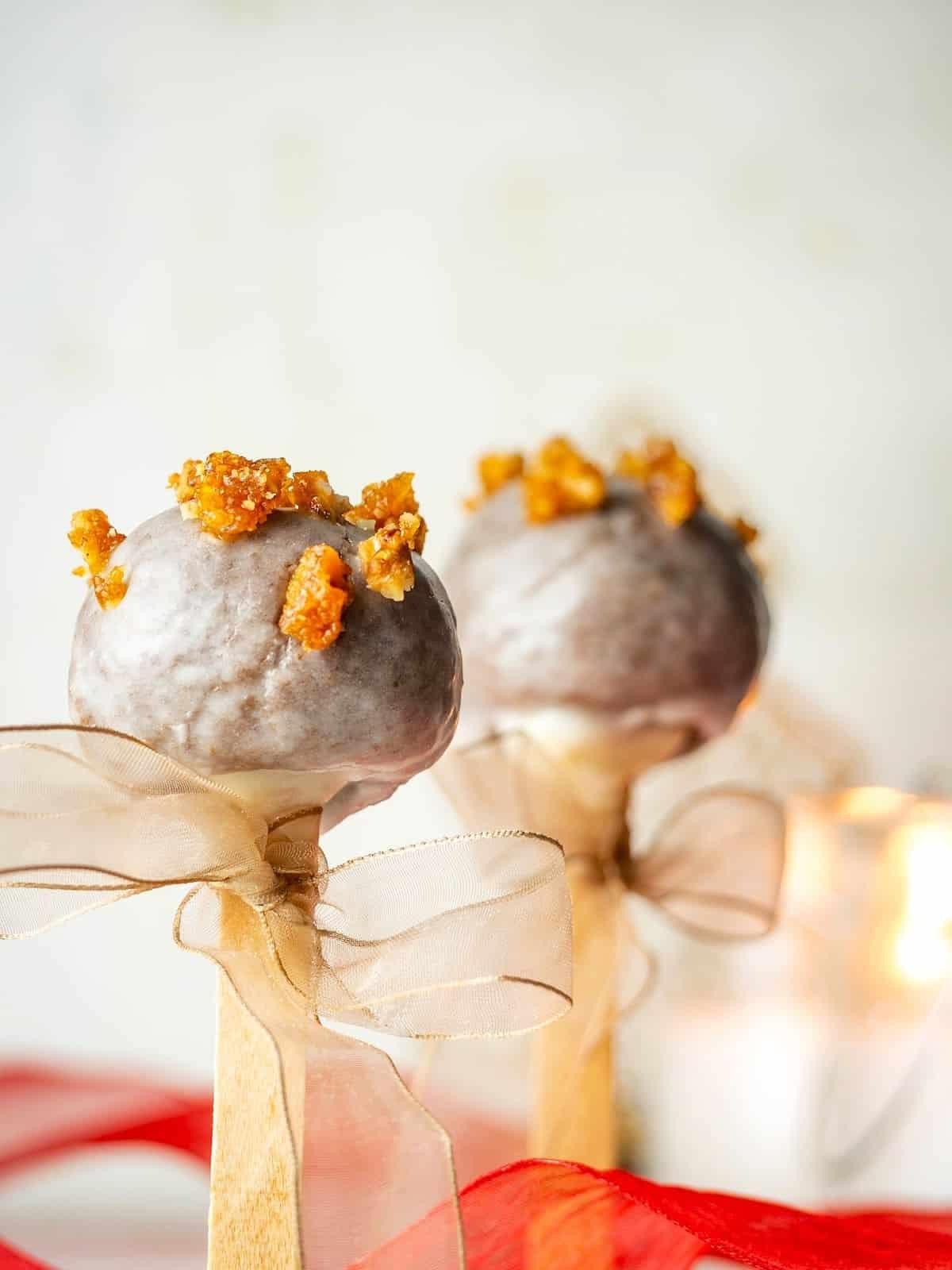 Sugar glazed covered cake pops on stick sprinkled with chopped pralines. 