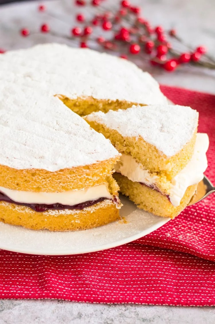 Portion take out from a sponge cake with cream and raspberry filling covered with icing sugar. 