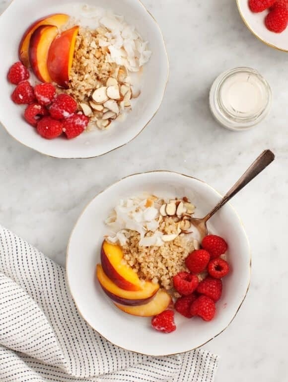 Tow bowls of quinoa served with slices of pear, fresh raspberries, cream and nuts.