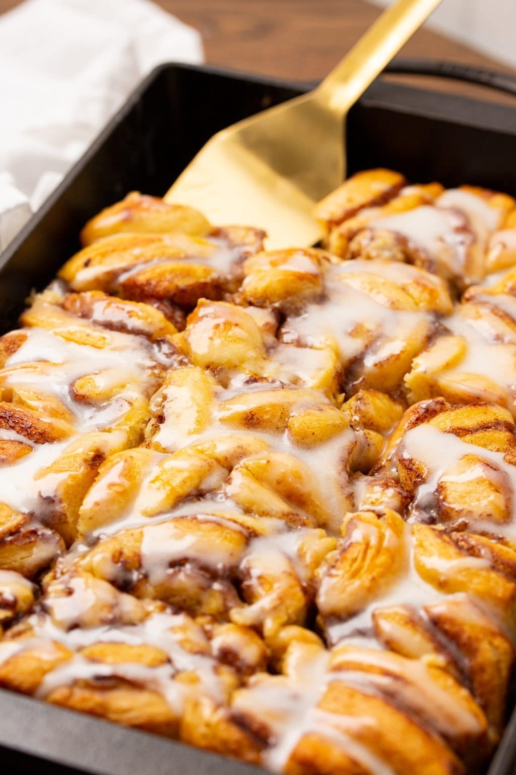 Golden spoon scooping a serving of cinnamon rolls with sugar glazed toppings cooked in a sheet pan.