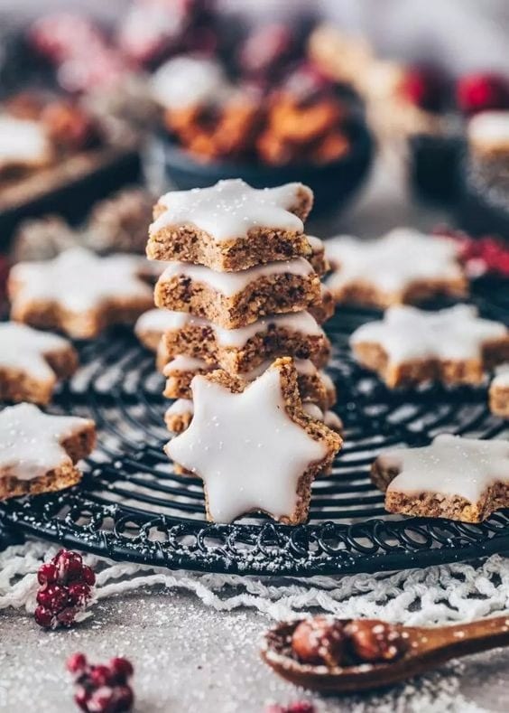 A stack of star shaped cinnamon cookies with frosting on top on a cooling rack. 