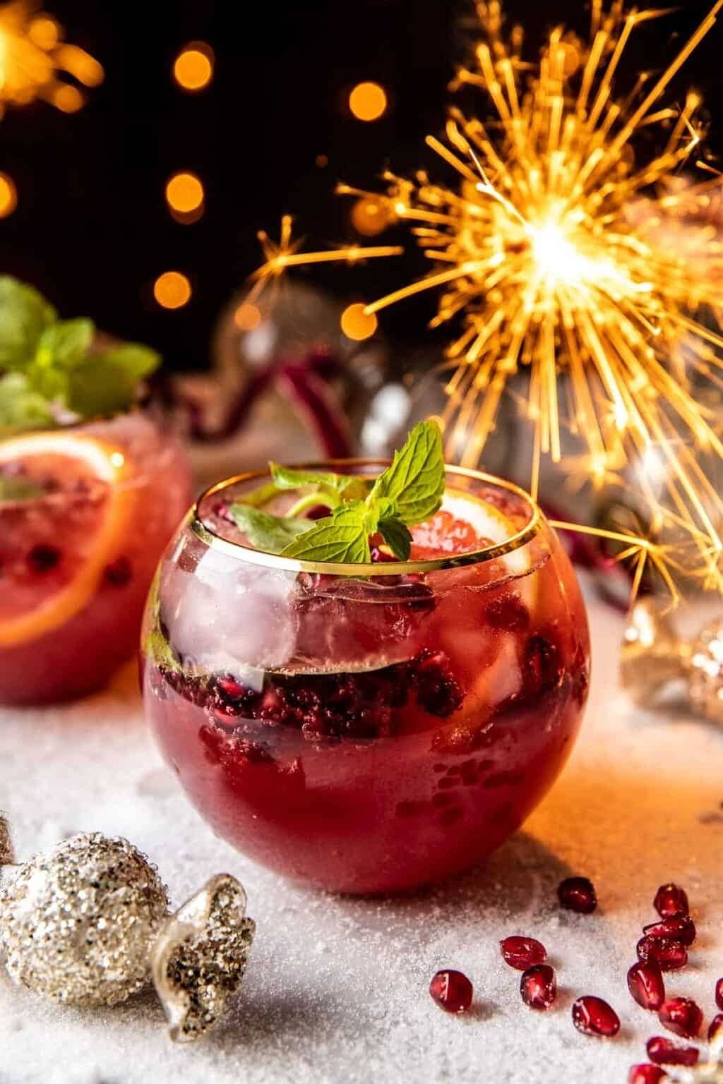 Pomegranate cocktail filled with ice, garnished with fresh pomegranate arils and slices.